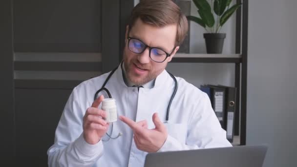 Doktor Brýlích Sedí Před Laptopem Drží Lahvičku Pilulek Ukazuje Palcem — Stock video