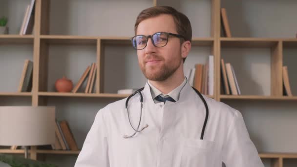 眼鏡とネクタイをかけた医師が本でいっぱいの棚の近くに立っています — ストック動画