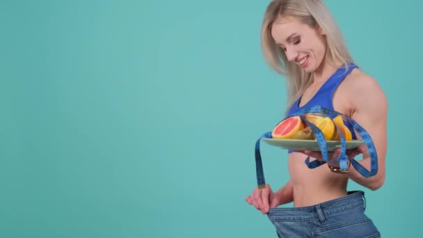 女性は彼女の体の形に対する懸念のジェスチャーを示し 手に果実のプレートで彼女の腰を測定しています — ストック動画