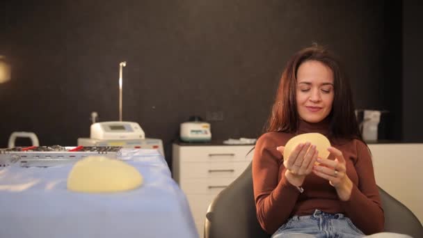 一位胸部尺寸较大的妇女正在拿着一个透明的轻型硅胶乳房植入物的复制品 — 图库视频影像