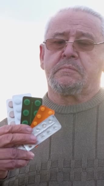 一个戴眼镜的男人手里拿着一堆药丸 他的面部头发和胡子补充了一张皱巴巴的脸 — 图库视频影像
