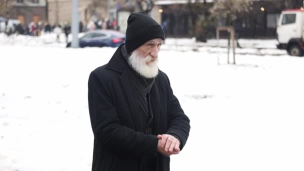 黒いアウターウェアの古い祖父は寒い冬の日に外に立っている間に手を温めている 街の背景にあるおじいちゃん — ストック動画