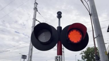 Kırmızı bir trafik ışığı, direği ve gökyüzünde bulutları olan. Yakınlarda dairesel otomobil parçası ve tekerlek kenarı olan bir ağaç var..