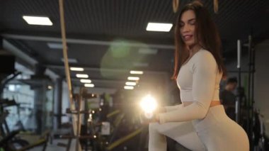 Spor salonunda, bir kadın elinde halterle oturur, bacaklarını güçlendirmek için kaslarını çalıştırır..