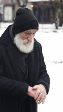 Yaşlı bir adam dışarıda soğuktan ellerini ovuşturuyor. Yaşlı bir adamın portresi kışın karla kaplı bir arka planda
