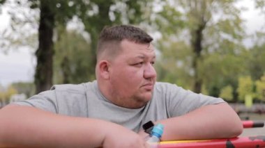 Açık havada yatay barın yanında duran aşırı kilolu adamın yüzüne yakın çekim. Antrenman sırasında mola. Fazla kiloyla mücadele et.