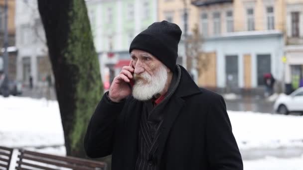 Öreg Szakállas Férfi Fekete Ruhában Telefonál Miközben Kint Áll Télen — Stock videók