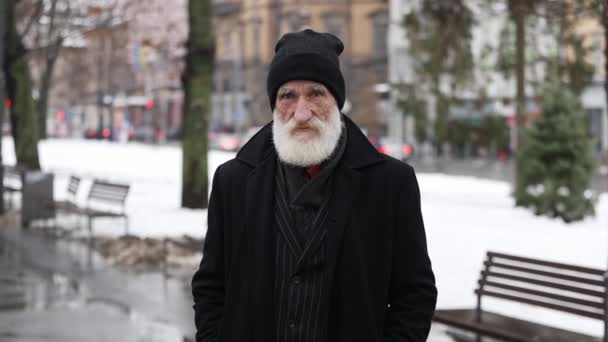 一位穿着黑色外套 满脸皱纹的老爷爷站在冬日的大街上挥动着食指 一个警觉的姿态 老人挥动着他的大拇指 — 图库视频影像