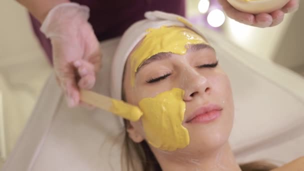 美容科医生在年轻漂亮女人的脸上涂上黄金海藻酸钠面罩 护肤程序 靠近点 — 图库视频影像