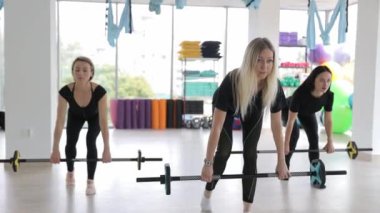 Spor giyimli üç kadın halter kaldırıyor, eğlenceli ve eğlenceli bir spor salonunda kollarını ve bacaklarını güçlendiriyorlar..