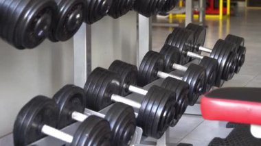 Spor salonundaki birçok siyah dambılın yakın çekimi. Antrenman için ağırlık. Spor malzemeleri. Bir kadın eğitim için dambıl alır.