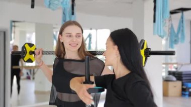 İki kadın spor salonunda halter kaldırmak için iş birliği yapıyor, eğlence ve spor müsabakalarının keyfini çıkarırken aynı zamanda eğleniyorlar..