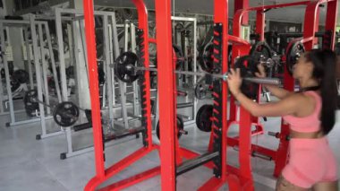 Pembe eşofmanlı seksi kadın vücut geliştirici spor salonunda halterlerle çalışıyor. Ağırlıklarla kuvvet egzersizleri.