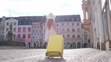 Beyaz elbiseli, güzel, zayıf bir kadın ve sarı bavullu güzel bir mimariyle şehir merkezinde yürüyor. Sofistike turist bayan.