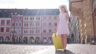 Beyaz şapkalı zayıf bir sarışın elinde sarı bir bavulla şehir merkezine doğru yürüyor. Bir Avrupa şehrinde bir turist.