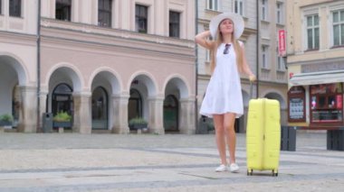 Beyaz elbiseli çekici bir turistin videosu antik mimarinin arka planına karşıdır. Sarı bavullu bir kadın yürüyor.