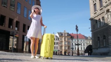 Şehir merkezinde güzel giyimli, güzel mimarisi olan, telefonda konuşan genç, zarif bir turist. Sarı valizli turist kadın..