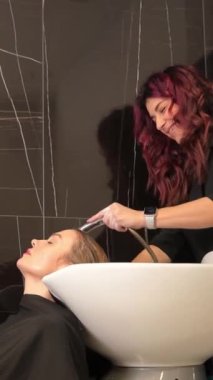 Bir kadın saçını kuaför lavabosunda yıkıyor, bir etkinliğe hazırlanıyor. Resmi kıyafetlerle rahatlarken parmakları kafa derisine masaj yapıyor..
