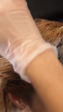 Eldivenlerle kaplı bir insan, nazikçe başka birinin saçını tarar..