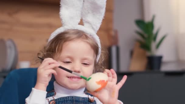 Mała Dziewczynka Króliczymi Uszami Maluje Wielkanocne Jajko Ręką Uśmiechem Twarzy — Wideo stockowe