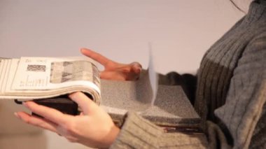 Kağıt kataloğu. Elinde katalog olan çekici bir esmer mobilya salonunda duruyor ve mobilyaları dikkatlice seçiyor. Salonda bir sürü ev eşyası var.