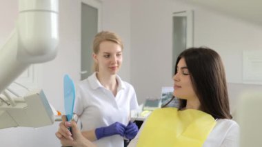 Güzel esmer bir kadın dişçi koltuğunda oturur ve aynaya bakar. Modern dişçilik. Diş tedavisinin sonucu
