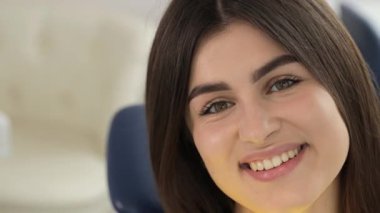 Güzel, kar beyazı bir gülümsemesi olan çok güzel, genç bir esmerin yüzüne yakın çekim. Dişçi koltuğunda beyaz dişli bir kız..