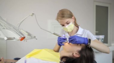 Bir dişçi, dişçi muayenehanesinde bir hastanın dişlerini kontrol eder. Tıp, dişçilik konsepti. Diş aletleri hastası, esmer.