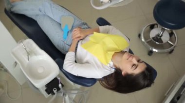 Tedaviden önce dişçi koltuğunda yatan genç bir kadının en iyi görüntüsü. Ağız boşluğundaki hastalıkların konforlu tedavisi.