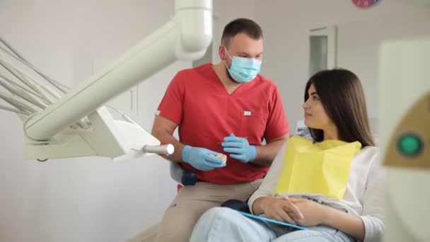 의사는 의자에 앉아있는 여성에게 플라스틱 보여줍니다 이빨로 구강의 레이아웃의 시각적 — 비디오