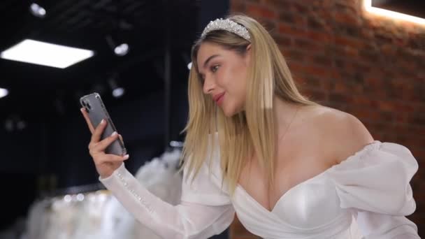 Panna Młoda Białej Sukience Robi Selfie Tle Innych Sukienek Salonie — Wideo stockowe