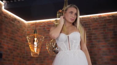 Gelin modeli beyaz bir gelinlik içinde tuğla bir duvarın ve lüks lambaların arkasında poz veriyor. Gelinlik reklamı çekimi. Gelin için lüks gelinlikler.
