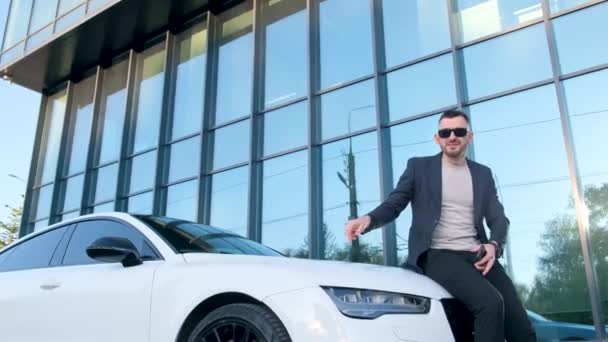 Güneş Gözlüklü Genç Bir Işadamı Beyaz Bir Arabanın Kaputunda Oturur — Stok video