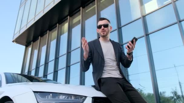 Güneş Gözlüklü Genç Bir Işadamı Beyaz Bir Arabanın Kaputunda Oturur — Stok video