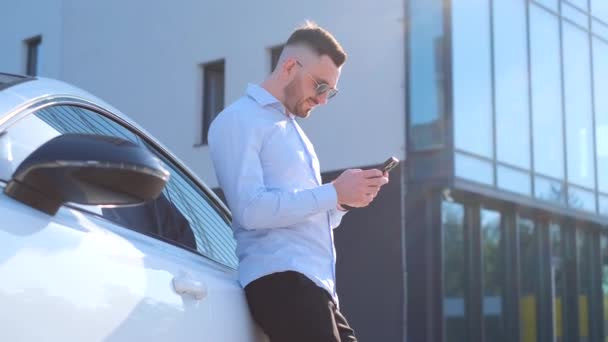 Güneş Gözlüklü Ince Bir Işadamı Pahalı Arabanın Yanındaki Telefona Bakıyor — Stok video