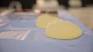 Masadaki göğüs implantlarının detaylı yakın plan çekimleri tıbbi ya da kozmetik amaçlar için çeşitli açıları gösteriyor. Anonim yazı tipi, elektrik mavisi, plastik, daire ve ahşap elementler