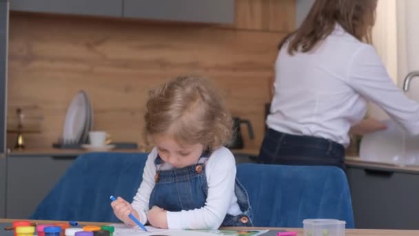 Mała Dziewczynka Tworzy Sztukę Przy Stole Znacznikami Podczas Gdy Kobieta — Wideo stockowe