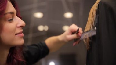 Uzun sarı bir kadın saçının yakın çekimi. Genç bir kuaför kuaför kuaför aletlerinin yardımıyla saç kesiyor..