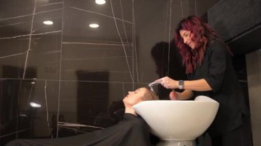 Güzellik salonunda kuaförlük prosedürleri. Bir kuaför müşterisinin saçını lavabonun altında yıkar. Profesyonel saç bakımı. Saç boyama işleminden sonra kafanı yıkamak..
