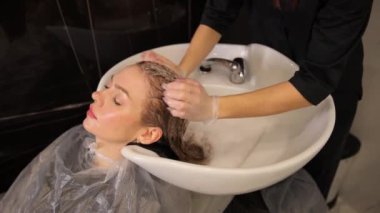 Kuaför kız müşterilerinin kafasını yıkar ve bir güzellik salonunda şampuanla yıkar. Boyama işleminden önce kafayı yıkamak. Profesyonel saç bakımı.