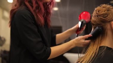 Bir kuaför bir kuaförde uzun sarı saçları saç kurutma makinesi ve yuvarlak bir fırçayla kurutur. Profesyonel saç bakımı.