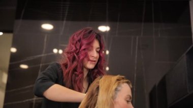 Lüks kıvırcık kızıl saçlı genç bir kuaför kız orta yaşlı bir kadının saçını boyama sürecinde. Gri saçlı. Saç boyası.