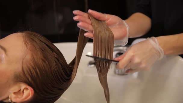 美容院の洗面台で女性の髪を閉じる ヘアドライヤーの手は クライアントの髪を洗い 結ばれた髪を櫛で結合します プロフェッショナルヘアケア — ストック動画