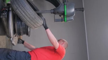 Kırmızı gömlekli bir adam garajda lastik eklemlerini sıkmak için kol kaslarını kullanıyor. El hareketleri, tekerlek üzerinde başparmağı ve dirseğiyle çalışırken konsantrasyonunu gösteriyor.