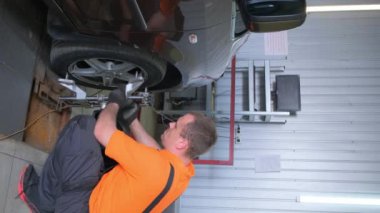 Bir adam garajda bir aracı tamir ediyor. Lastik ve tekerleği değiştirmeye çalışıyor. Otomotiv aydınlatmasını ve dışını kontrol ediyor. Çamurluğu ve otomobil tekerlek sistemini tamir ediyor.