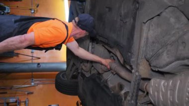 Otomobil parçaları ve ahşap döşeme kullanarak bir garajdaki araç kapısını tamir eden bir adam. Araba üzerinde çalışırken başparmağı arabanın dış kısmına bastırıyor.