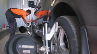 İki adam garajda bir motorlu aracı tamir ediyor. Lastik yerine alaşımlı tekerlek takıyorlar. Araç çamurluğunda çalışıyorlar ve sentetik kauçuktan yapılmış lastik izlerini kontrol ediyorlar.