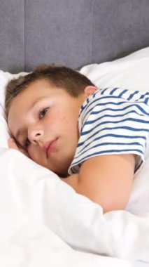 Genç bir çocuk, beyaz çarşaflı, burnu hafifçe yastığa değen, başparmağını rahatlamak için kalçasının altına sıkıştırılan bir yatakta huzur içinde uyuyor.