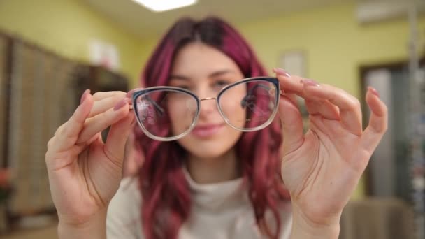 美しい赤いカーリーの髪を持つ少女は 視力を向上させるためにメガネを選択します ビジョン訂正 光学店でのプロのメガネの選定 — ストック動画