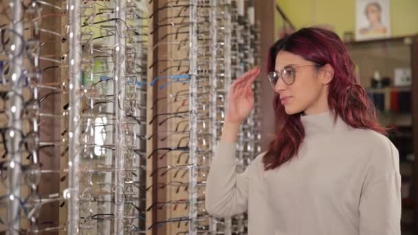 Młoda Amerykanka Wybiera Ciemne Okulary Stojąc Tle Gabloty Okularami Specjalistyczny — Wideo stockowe